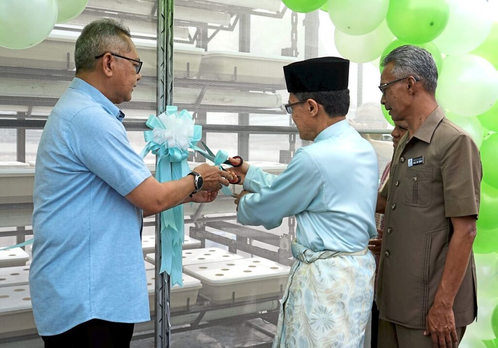 Mosque chairman Dr Abdullah Ismail (centre) cutting a ribbon in accepting the rotation hydroponic system with Shamsul Bahar (left) and Temerloh Municipal Council president Suris Mihat.